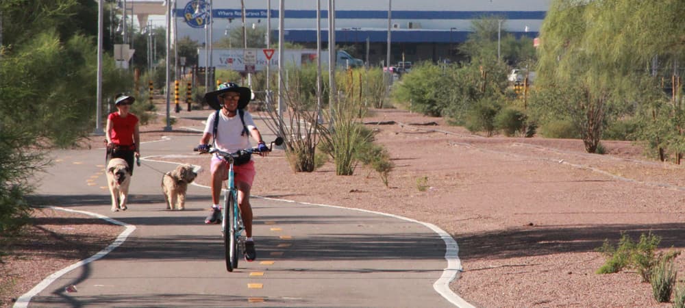 A woman rides a bicycle and another walks two dogs on the Loop in Tucson, AZ.