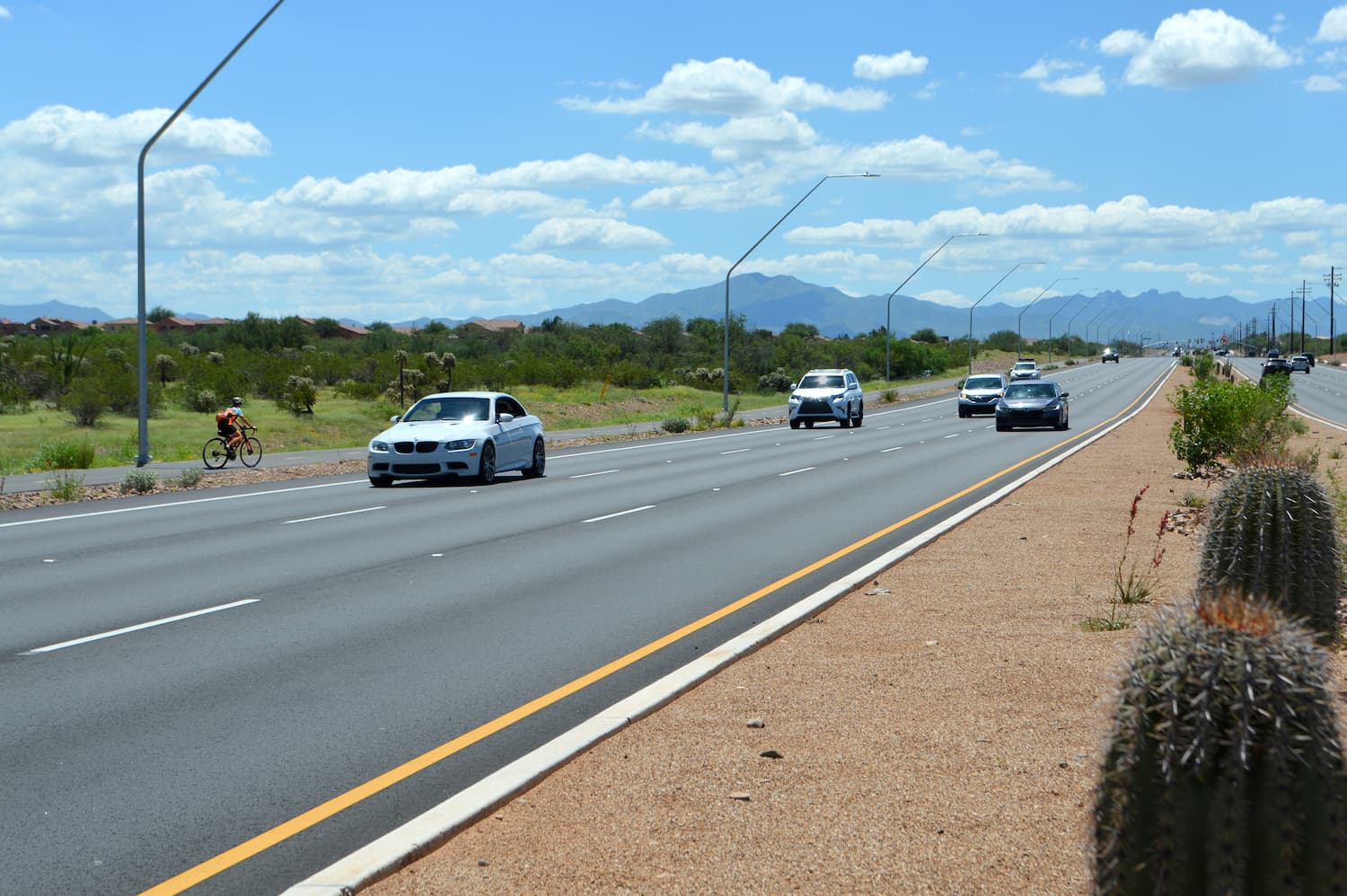 Houghton Rd in Tucson, Arizona with several cars driving. A cyclist is riding on the bike path adjacent.