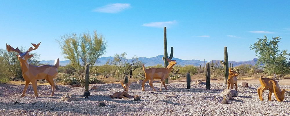 A metal polygonal sculpture of deer grazing in the desert.