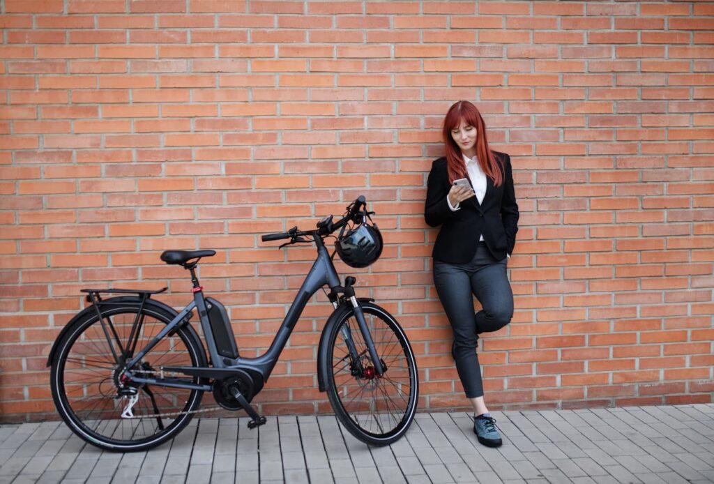 Portrait of businesswoman commuter on the way to work with bike, using smartphone.