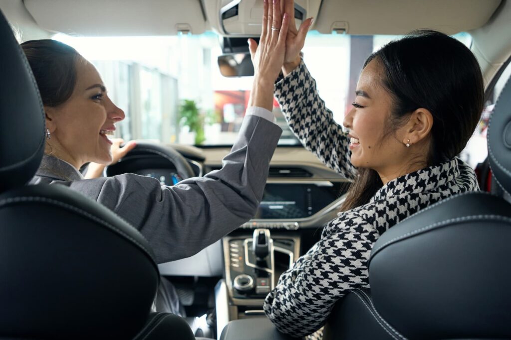 Two happy women giving each other high-five sitting in a car.