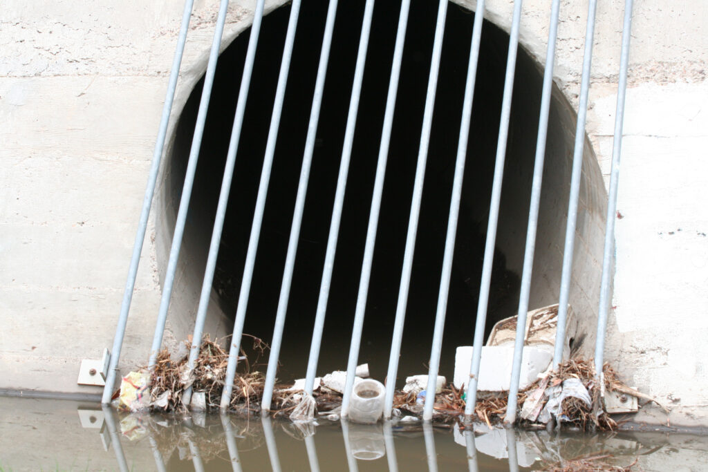 A storm drain clogged with debris and trash.