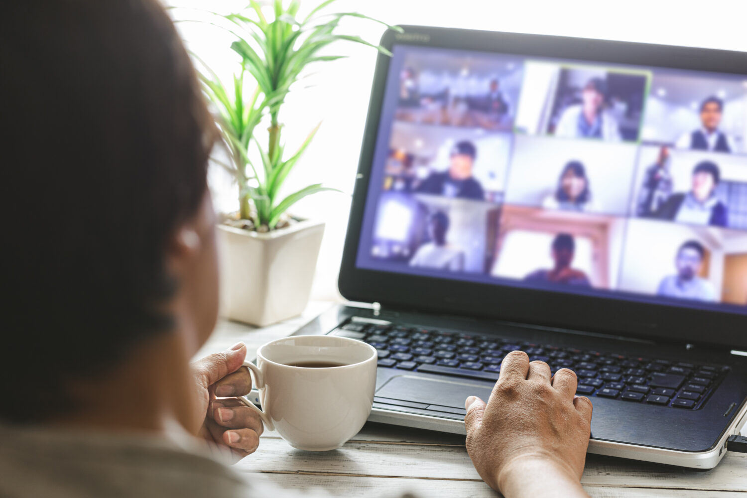 Employee participates in a Zoom meeting on a laptop while drinking coffee.